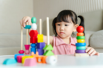 3 year old girl having fun playing with colorful geometric shape wooden blocks educational toys at...