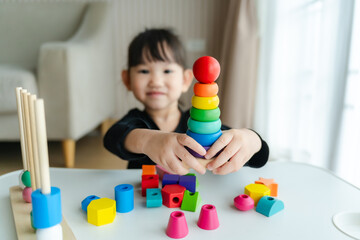 3 year old girl having fun playing with colorful geometric shape wooden blocks educational toys at...