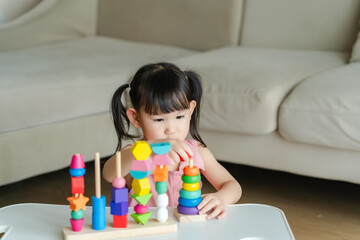 3 year old girl having fun playing with colorful geometric shape wooden blocks educational toys at...