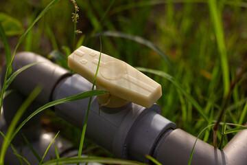A close-up view of a light-colored plastic valve on a grey PVC pipe, surrounded by lush green grass...