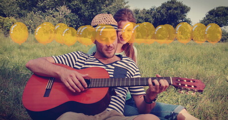 Image of balloons icons over happy caucasian couple playing guitar