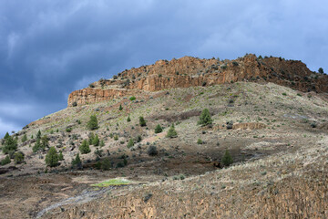 Fototapeta premium Rocky cliffs highlighted by sun on a stormy cloudy day, John Day National and Scenic River landscape from Service Creek campground, as a nature background 