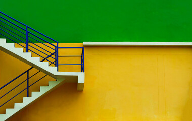 Modern staircase with blue railing against vibrant green and yellow wall, minimalist urban architecture, Emergency exit highlight minimalist architecture Clean structure of the building exterior.