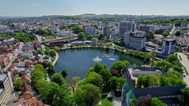 Smooth drone pan around Breiavatnet showcasing the beautiful central fountain and Stavanger&rsquo;s high-rise buildings in the background on a sunny day.