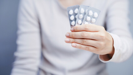 Person holding three blister packs of white round pills, close up, healthcare and medication concept