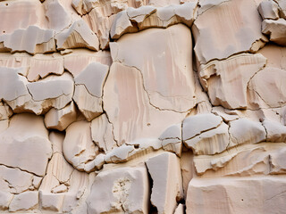 Close-up of a weathered sandstone rock face with cracks and rough texture, showcasing natural patterns and geological formations in a beige color palette