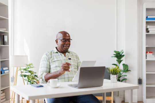 Busy mature middle aged business man, senior man in workplace reading Documents and work onlaptop computer sitting at work desk in office
