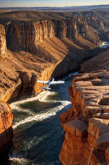 small modern airplane flying in deep rocky canyon with swiftly moving river beneath