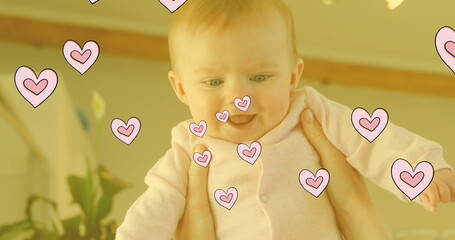 Image of falling hearts over happy caucasian happy baby