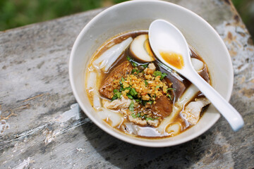 Pork noodles in a ceramic bowl placed on a wooden table with space for copying.