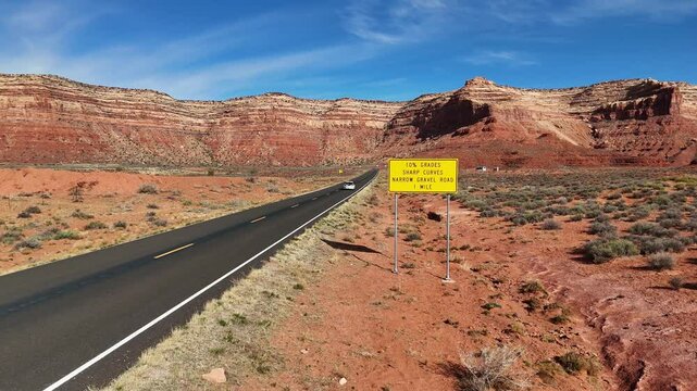 Car driving down desert road with bike rack on the back and Tall Red Cliffs in the background. Utah State Route 261