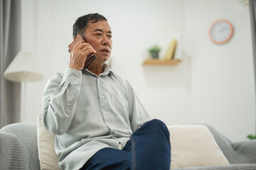 Thoughtful senior man speaking on mobile phone in cozy living room, engaged in conversation, expressing focus and interest, home environment