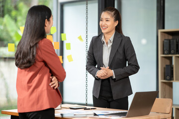 Two Asian businesswomen sit in a meeting discussing presentation ideas in an office.