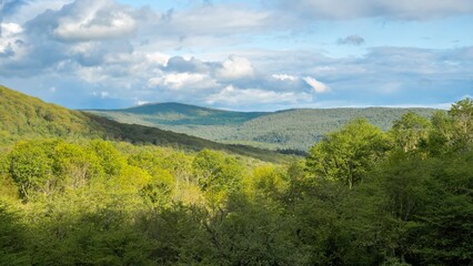 Beautiful rolling hills, green forest, valley and blue sky with clouds casting shadows on the rural landscape on a summer day. Catskill Mountains, New York State, USA.