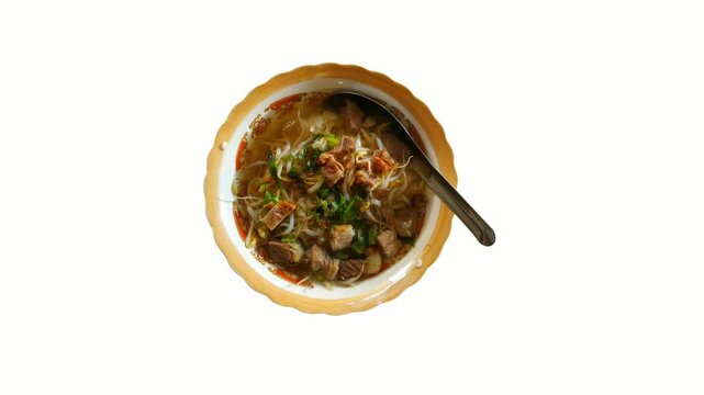 Top view of a traditional Indonesian beef soup, Soto Kwali, served in a vintage enamel bowl with rich broth, bean sprouts, herbs, and tender beef chunks.