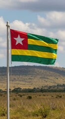Waving Togolese Flag Representing West African Heritage Over the Rolling Savanna Hills Landscape