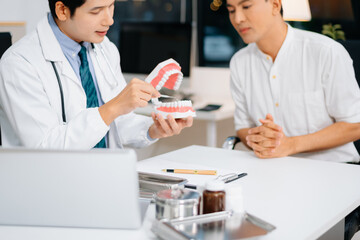 Fototapeta premium Asian dentist explains oral care using dental jaw model to male patient in clinic. Concept of dental hygiene, checkup, health education,