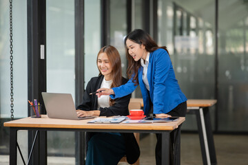 Fototapeta premium Two Asian businesswomen using laptops, on the table there are graph documents working on business investment.