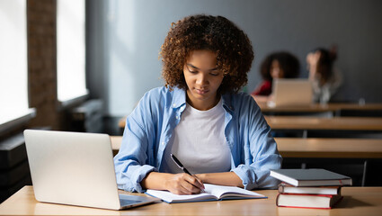 Focused female student studying in a classroom with laptop and books