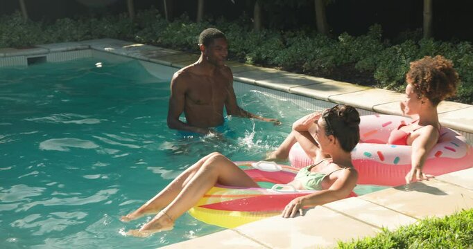 Diverse friends enjoying pool time, laughing and relaxing on floaties in sunny backyard