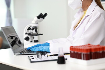Scientist in laboratory analyzes blood sample using microscope and test tubes. Biotechnology,...