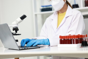 Scientist in laboratory analyzes blood sample using microscope and test tubes. Biotechnology,...