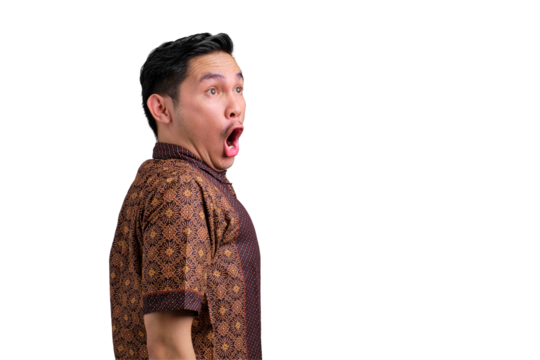 Shocked young Asian man in batik shirt looking away with opened mouth isolated on transparent background