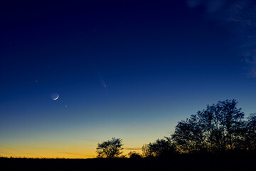 Crescent young Moon with stars, planets and countryside silhouettes.