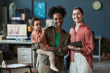 Portrait of smiling multigenerational family standing in modern office environment, holding a baby, while sharing moment of joy and bonding captured in warm light