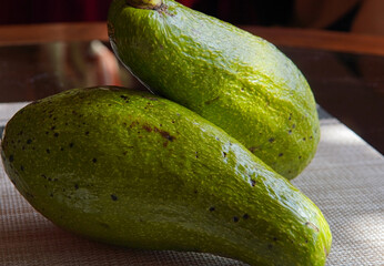 Two avocados on a wooden and glass table with a rustic and country background