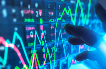 Hand interacting with financial data on a digital screen showing stock market graphs
