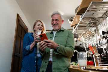 Senior couple laughing and using a smartphone in the kitchen at home