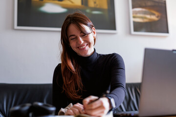 Brunette woman smiling while writing notes in a cozy home office setting