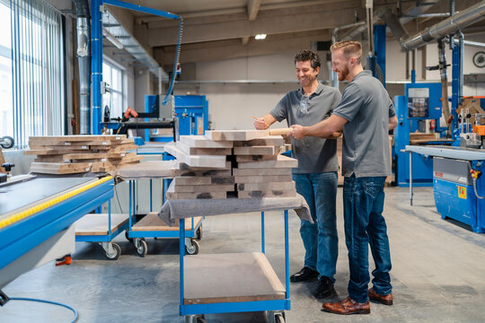 Two carpenters examining wooden planks in production hall