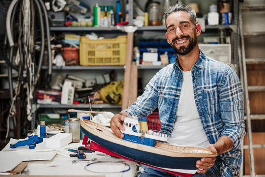 Smiling male craftsperson holding ship model at workshop