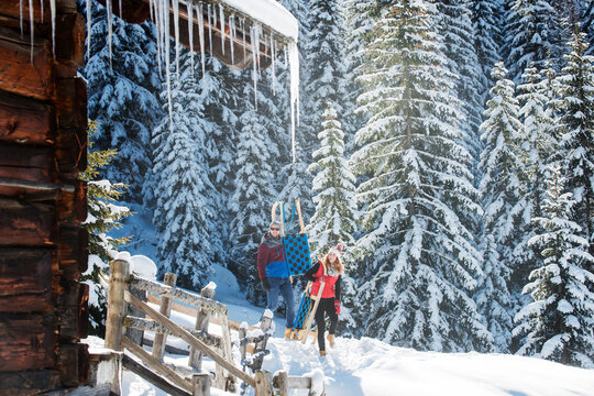 Man and woman with toboggan walking by pine trees during winter