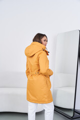 Fototapeta premium Woman wearing yellow coat and boots standing in modern indoor space with mirror