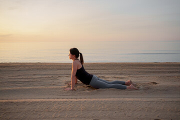 Woman practicing yoga on the beach at sunrise