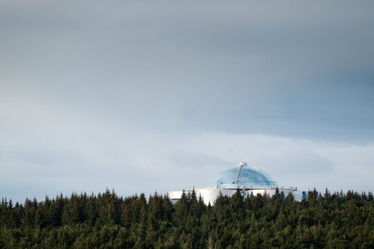 Perlan museum emerging from icelandic forest under cloudy sky