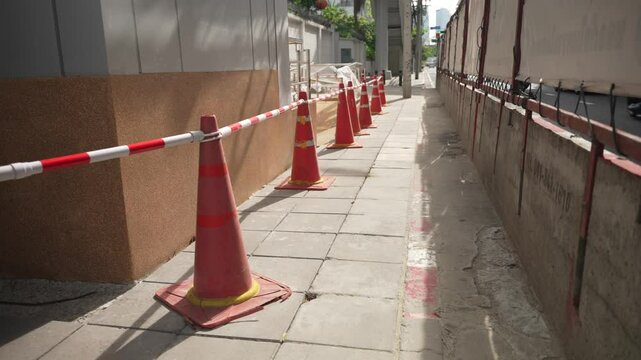 Close up of orange traffic cones and red-white barrier indicating maintenance area during daylight on city street sidewalk 