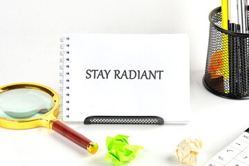 A workspace setup features a notebook displaying the words Stay Radiant alongside colorful paper...