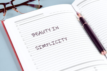 A red notebook opens to a blank page showcasing the phrase beauty in simplicity, accompanied by a...