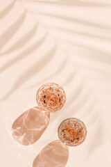 Top view two glasses of rose wine on pastel pink background with palm leaf shadow and sun glare. Clear wineglass minimal photo, closeup sparkling alcohol drink, aesthetic still life summer drink
