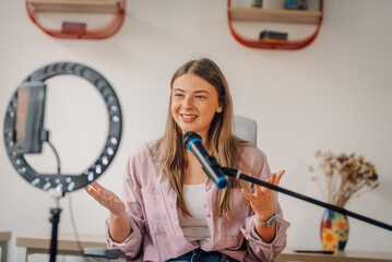 Young woman recording podcast using microphone and ring light