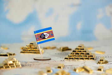 Naklejka premium Eswatini flag prominently displayed among numerous shimmering gold bars on a world map, representing national wealth, economic growth, and global trade