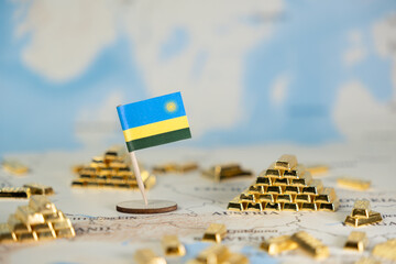 Rwanda national flag standing on a global map surrounded by miniature gold bars, symbolizing...
