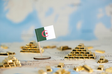 Algerian flag positioned among miniature gold bars on a blurred global map, representing national...
