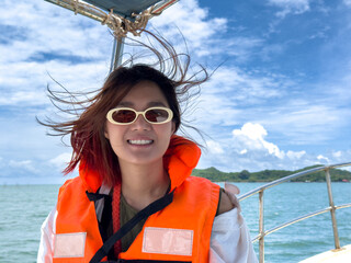 Happy asian Thai woman wear sunglasses and orange life jacket, smiling while traveling on boat to...