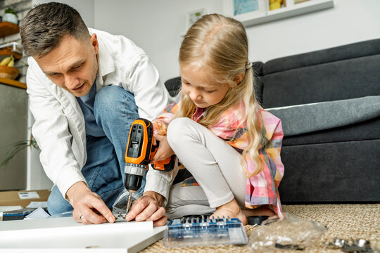 Father and daughter assembling furniture together crouching on floor