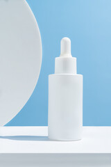 White unbranded dropper bottle on white podium against blue background. Skin care product presentation. Trendy showcase